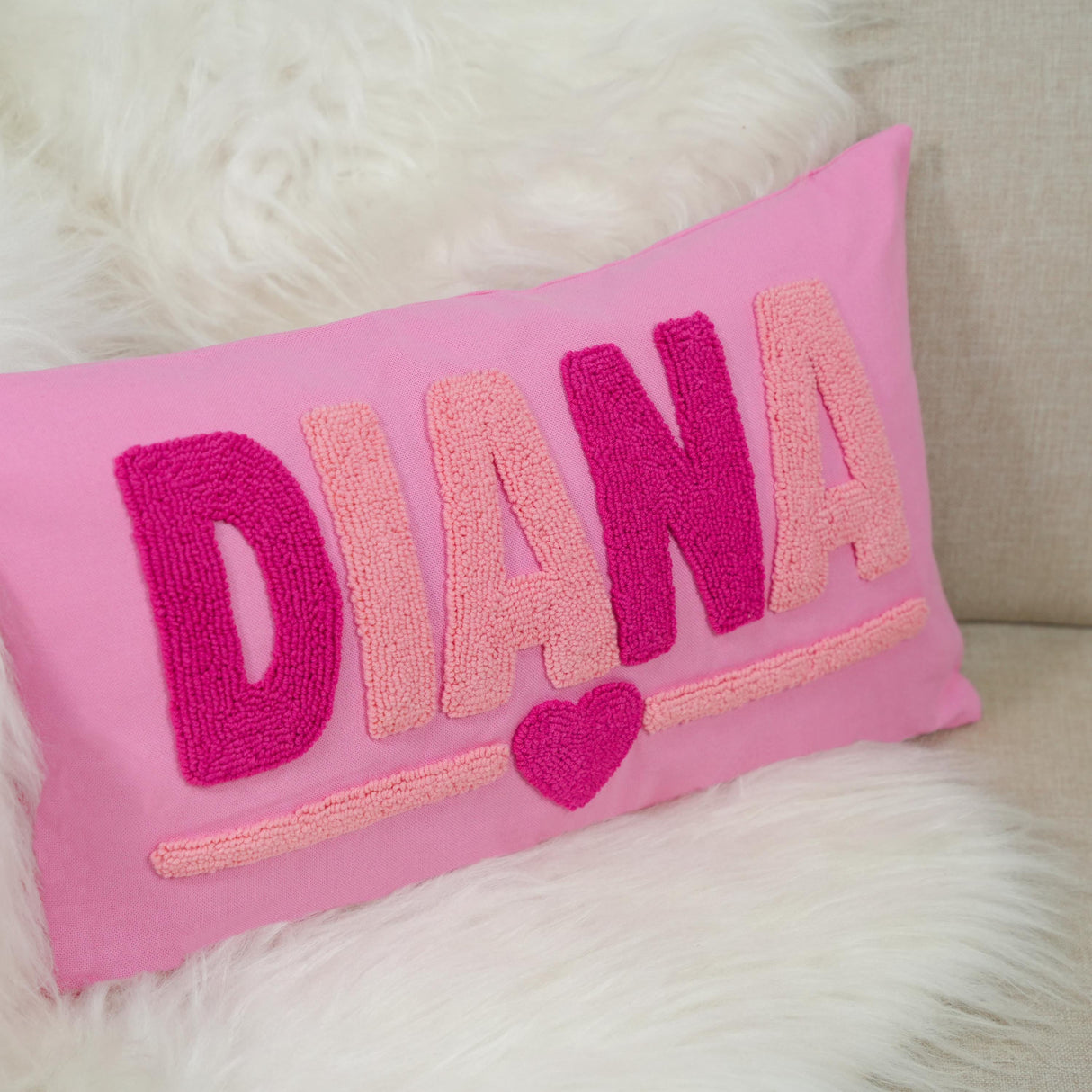 A pink pillow with the name "DIANA" embroidered on it, along with a heart symbol.