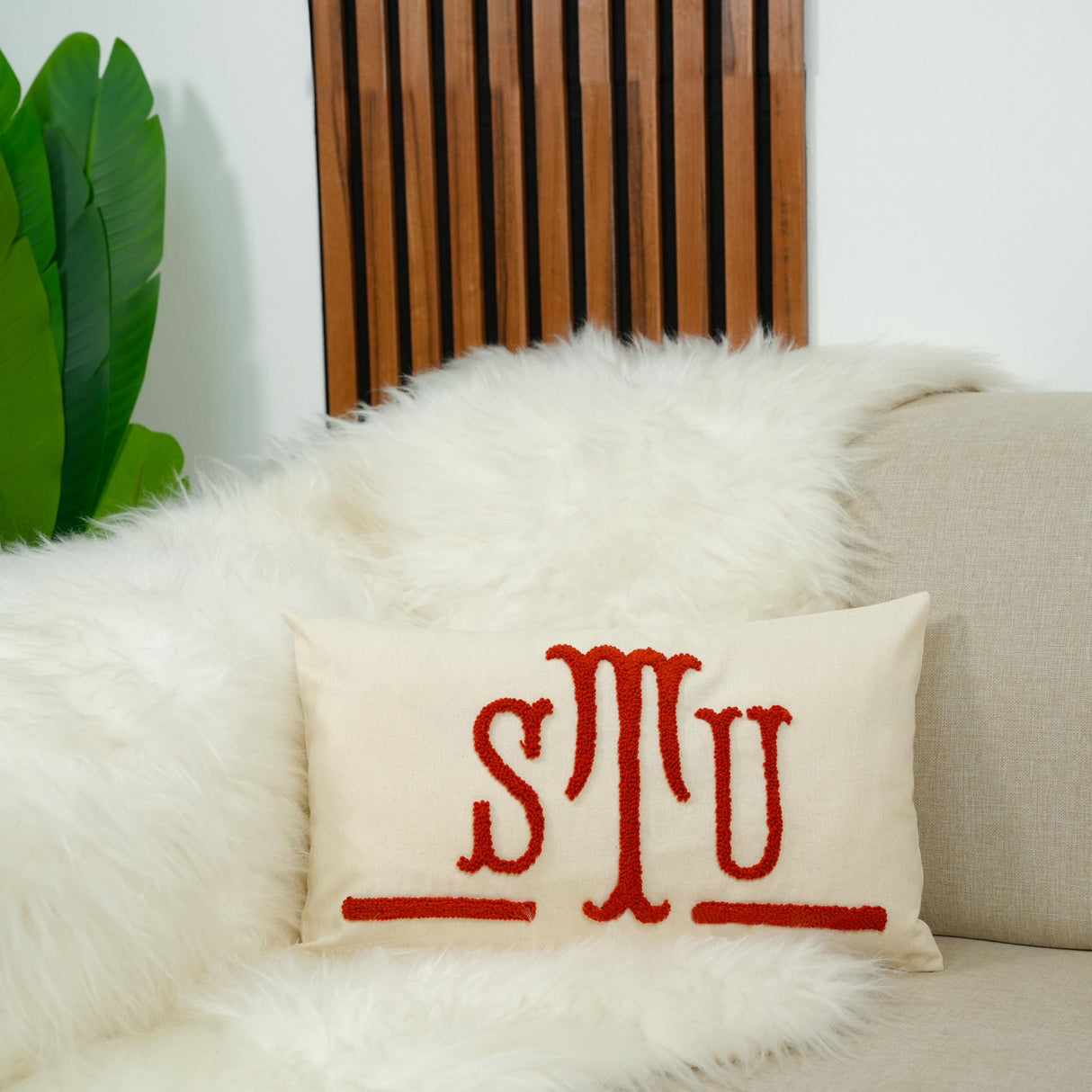 A white fur throw pillow with the initials "S.T.U." embroidered on it, placed on a beige couch.