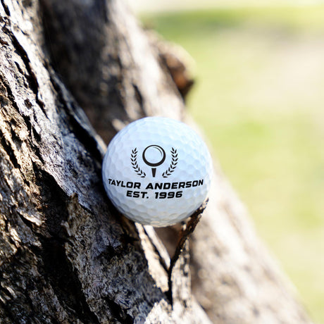 Golf ball with 'Taylor Anderson' branding against a tree trunk
