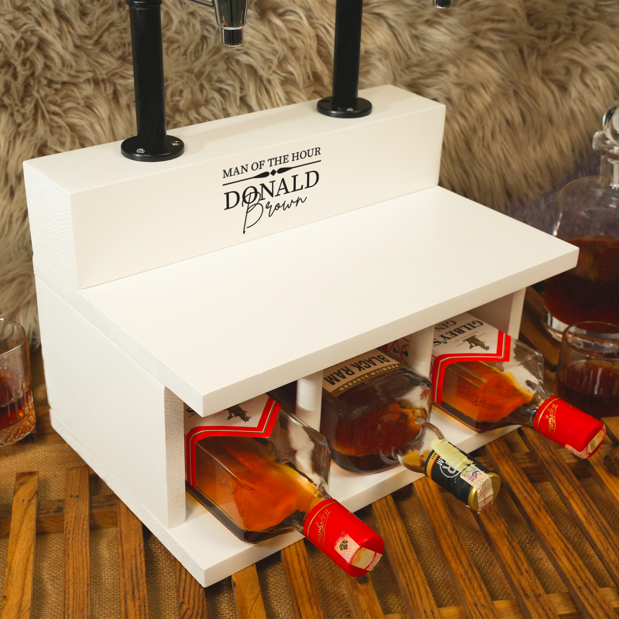 White bar cart with bottles of alcohol and 'Man of the Hour Donald' sign on a wooden surface.