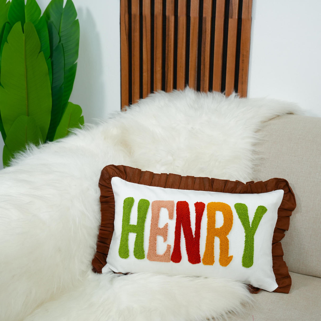 A white fur throw pillow with the name "HENRY" embroidered on it, placed on a white couch.