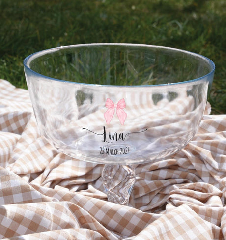 A clear glass bowl with a pink bow on it, placed on a checkered cloth.