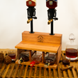 Wooden bottle holder with four bottles and two glasses on a wooden surface.