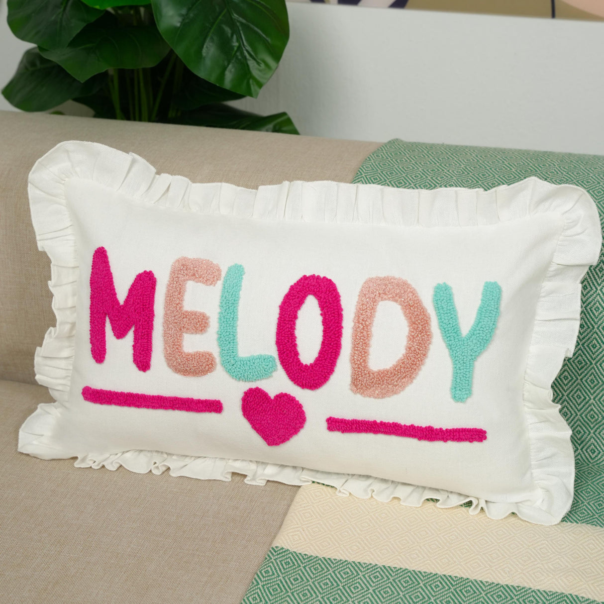 A white pillow with the word "Melody" embroidered on it, sitting on a couch.