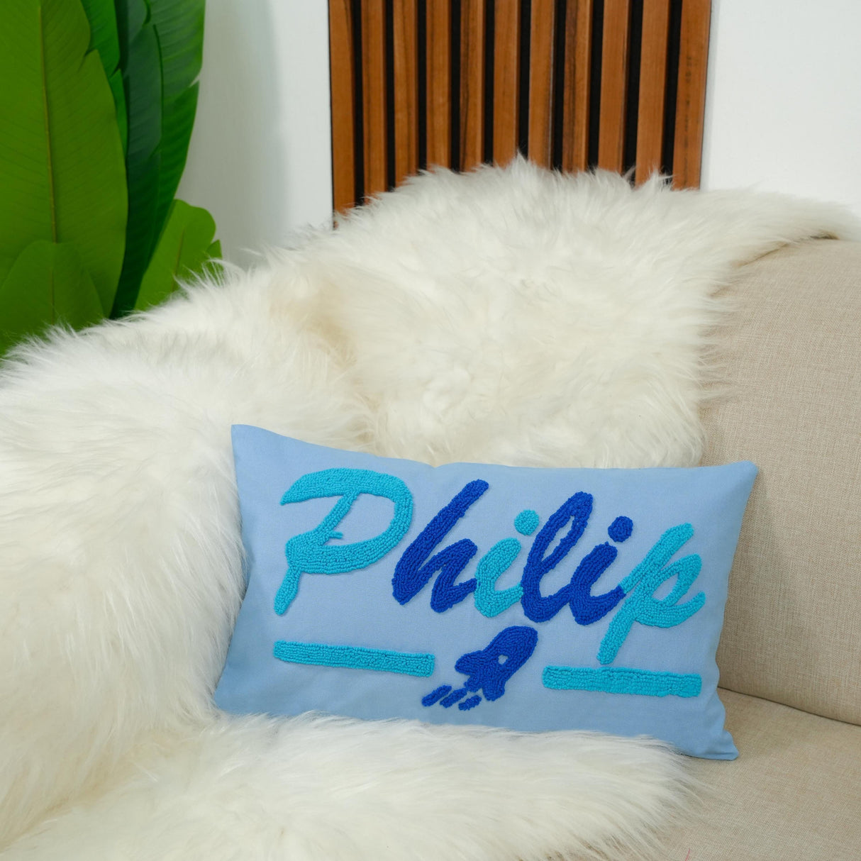 A blue throw pillow with the name "Philip" embroidered on it, placed on a white fur-covered couch.