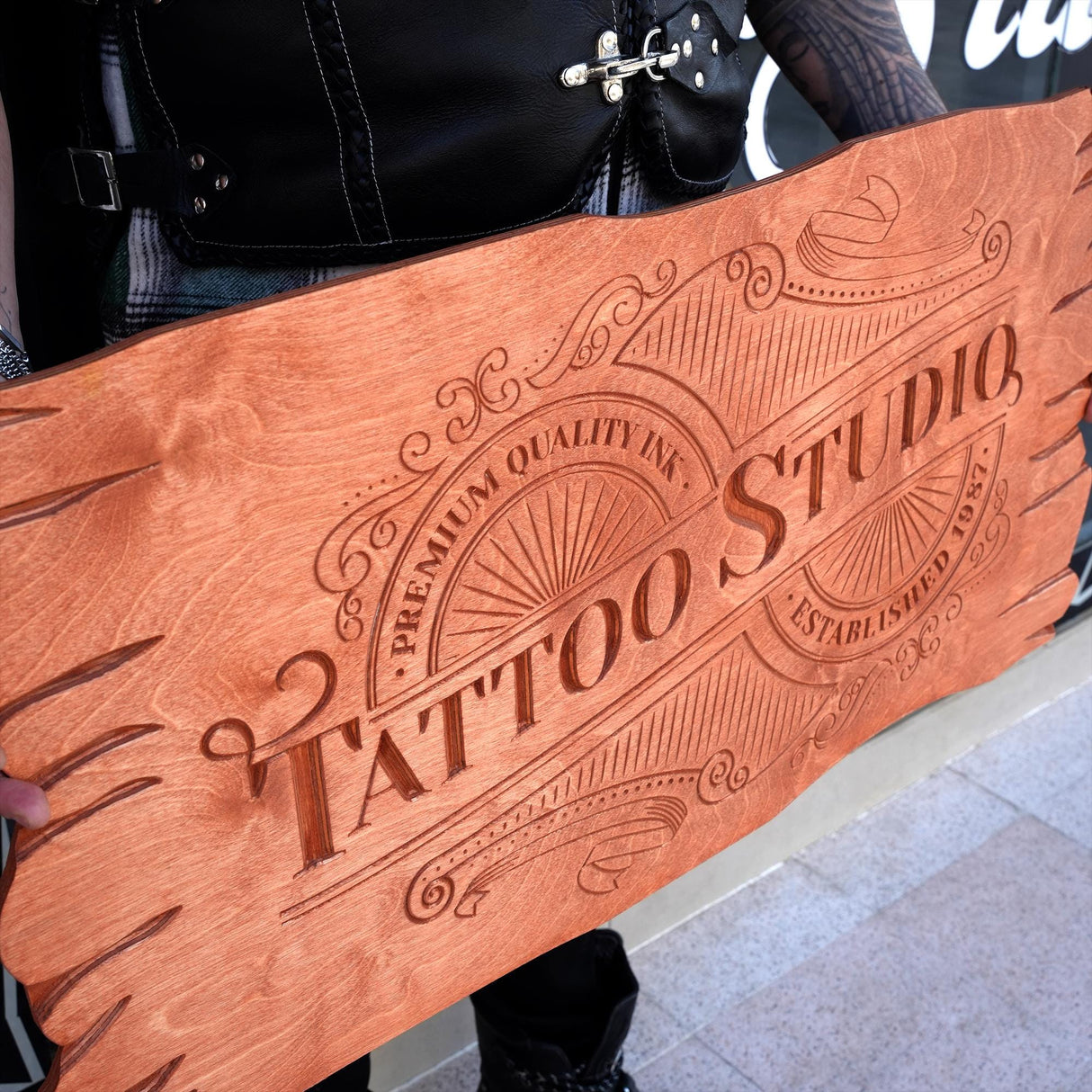 a person holding a wooden sign that says tattoo studio