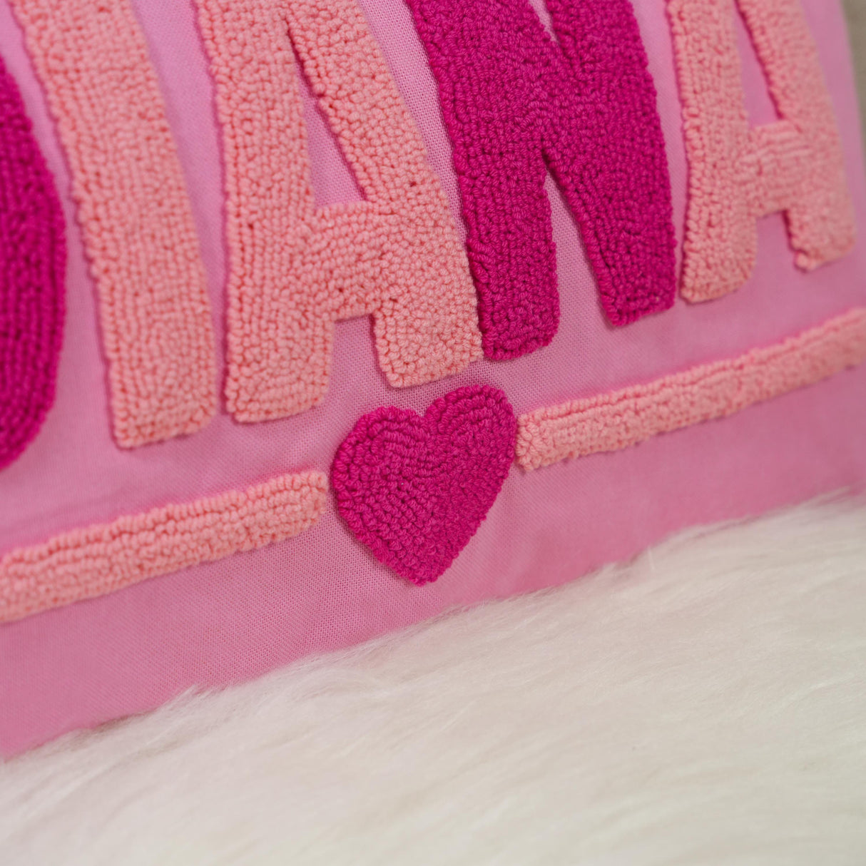 A close-up image of a pink and purple textured pillow with a heart-shaped embroidered patch in the center.