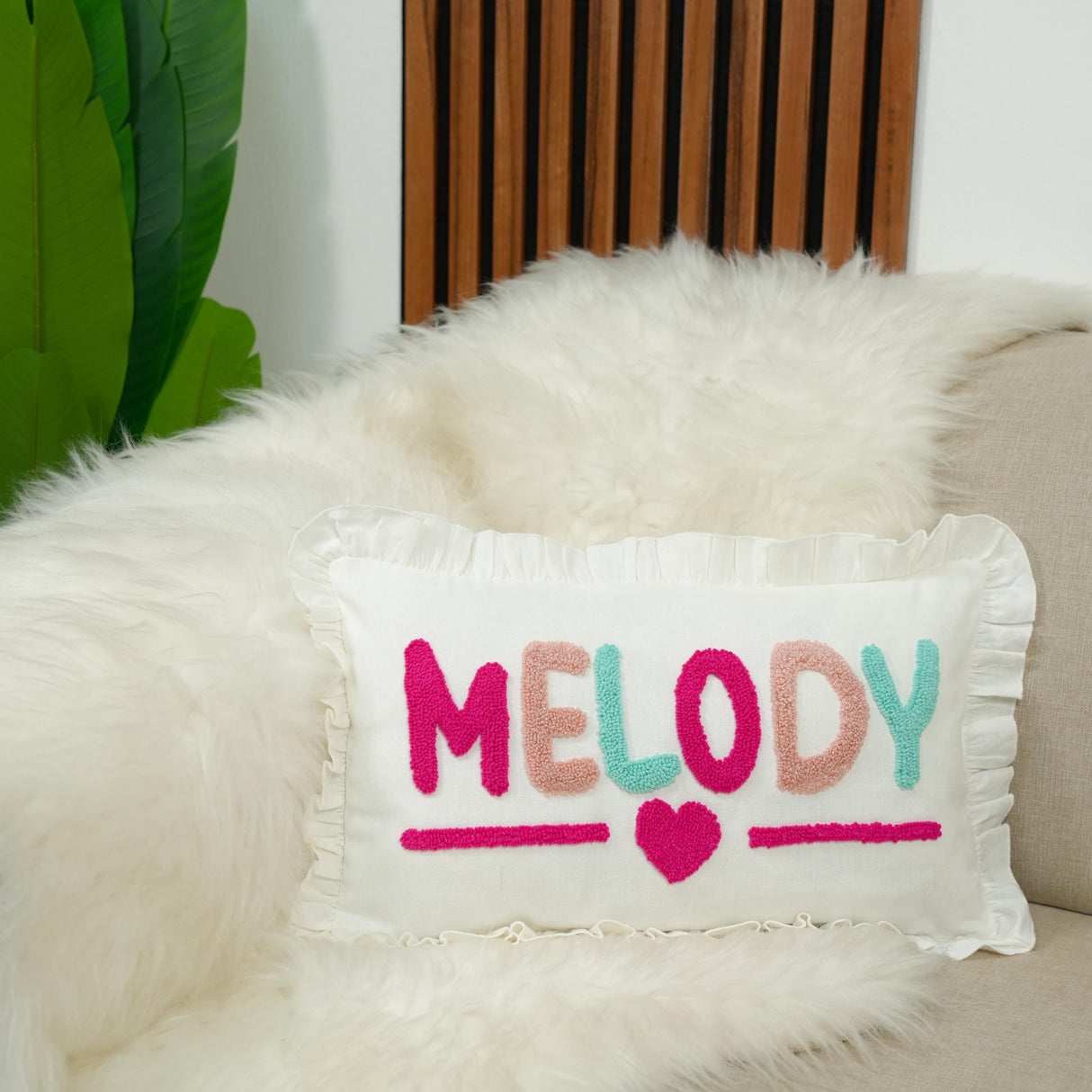A white fluffy pillow with the word "MELODY" embroidered on it, placed on a couch.