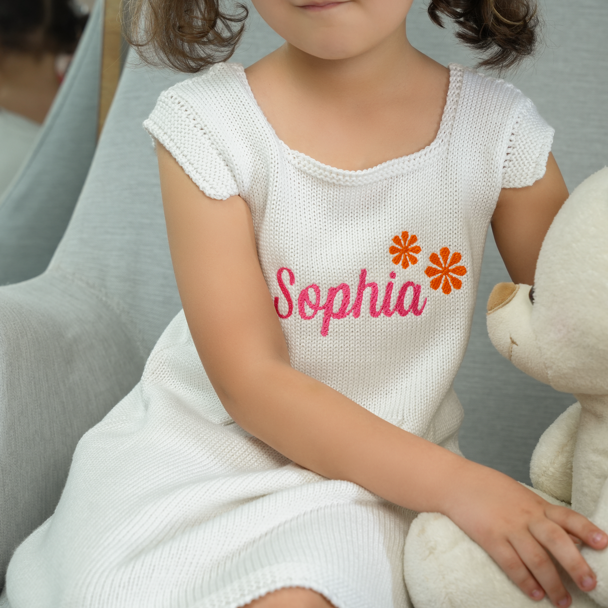 a girl in a white dress sitting on a gray armchair