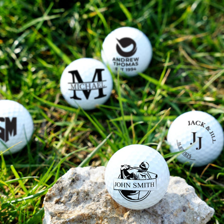 Personalized golf balls with various designs and text on grass and a rock.
