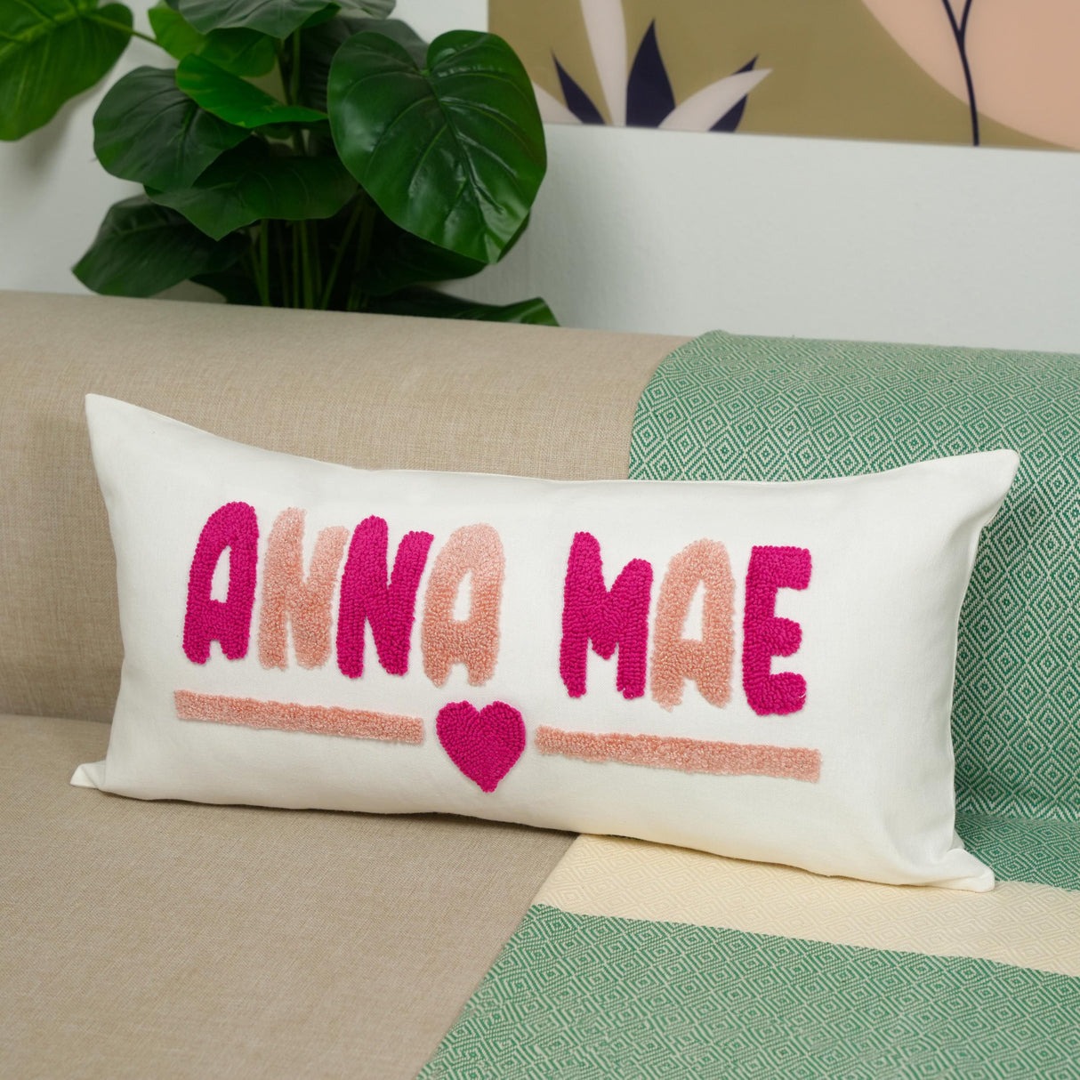 A white pillow with pink and purple embroidered text and a heart shape sits on a couch.