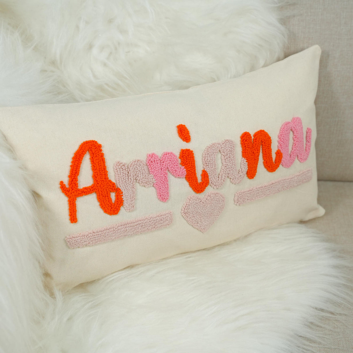 A white pillow with the name "Ariaana" embroidered on it in pink and orange colors.