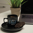 a cup of coffee with a cookie on a plate next to a laptop
