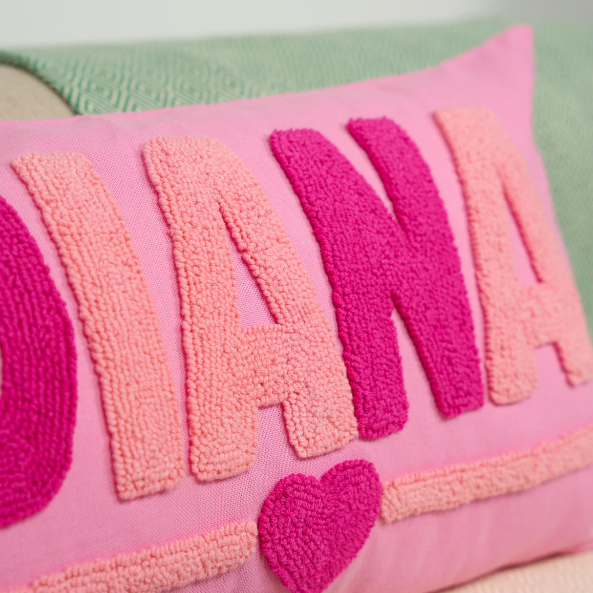 A close-up image of a pink and green textured pillow with the word &quot;DIANA&quot; prominently displayed in large letters.