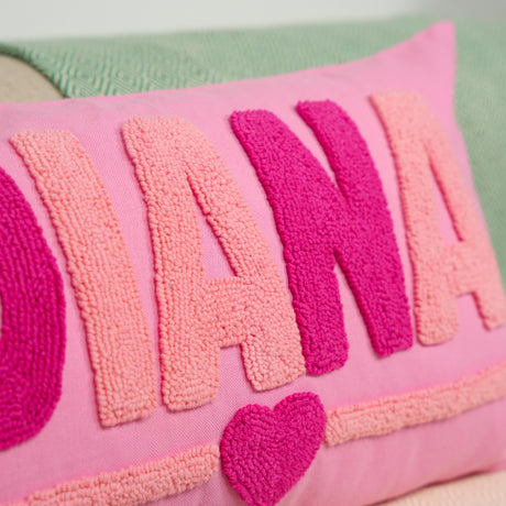 A close-up image of a pink and green textured pillow with the word &quot;DIANA&quot; prominently displayed in large letters.