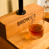 Glass of whiskey on a wooden coaster with 'Brown's' branding.