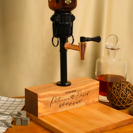 Wooden beer pump with engraved text on a wooden block, next to a glass decanter with liquid.