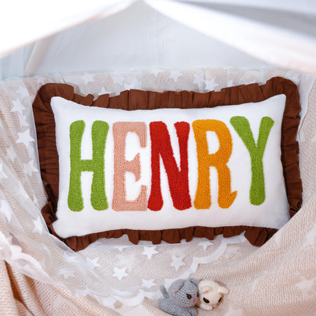 A decorative pillow with the name &quot;HENRY&quot; embroidered on it, placed on a bed with a white lace blanket.
