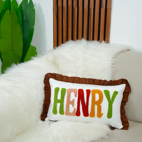 A white fur throw pillow with the name &quot;HENRY&quot; embroidered on it, placed on a white couch.