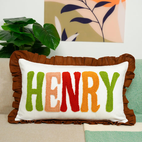 A decorative throw pillow with the name &quot;HENRY&quot; embroidered on it, placed on a couch.