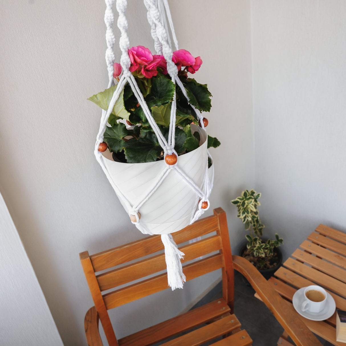 a white hanging planter with pink flowers in it