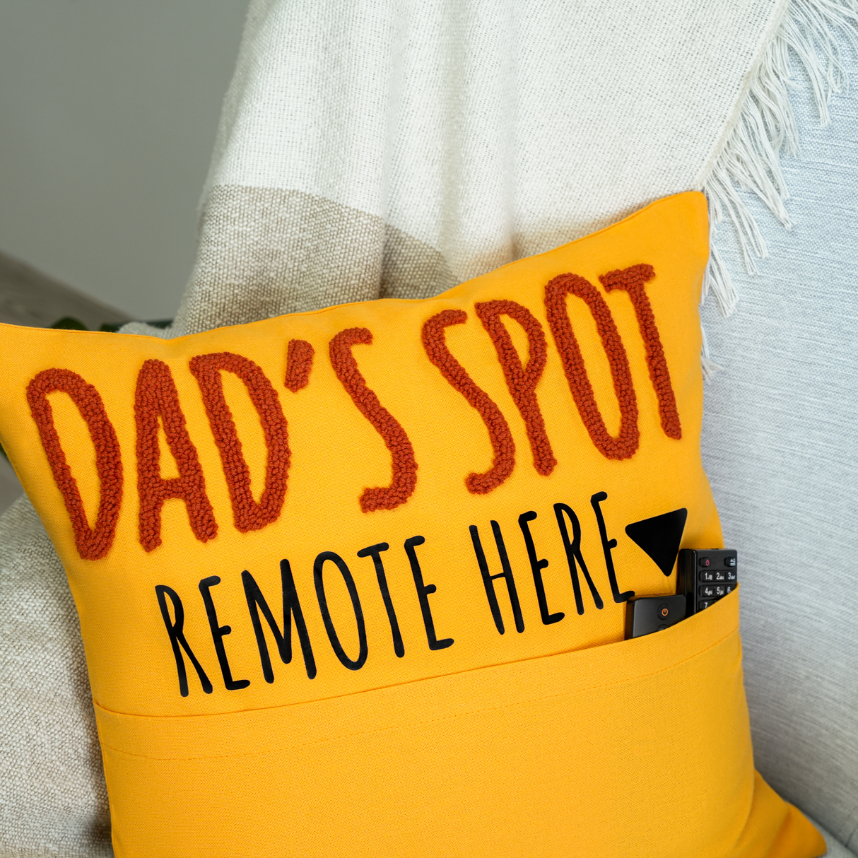 a yellow pillow that says dad's spot remote here