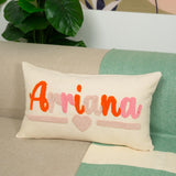 A white pillow with the name &quot;Arriana&quot; embroidered on it, sitting on a couch with a green and white patterned blanket underneath.