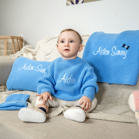 a little boy sitting on a couch wearing a blue sweater