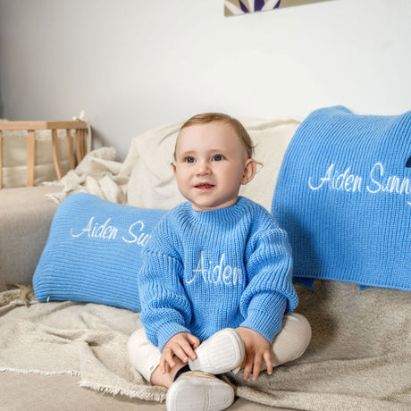 a baby sitting on a couch wearing a blue sweater