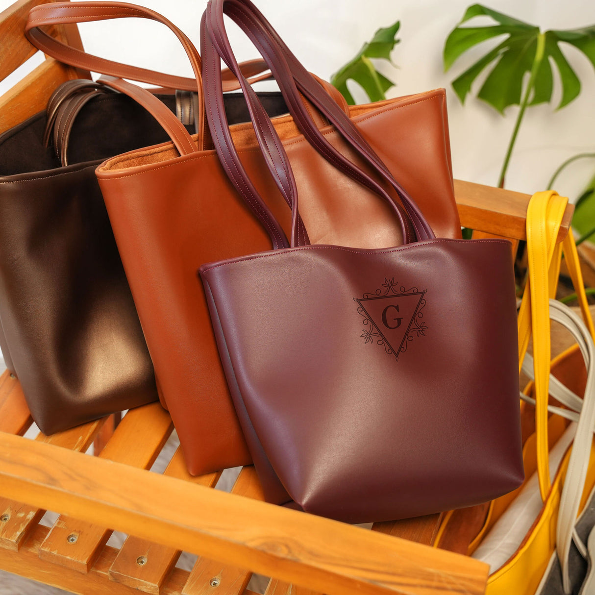 Trio of leather tote bags in different colors with monogrammed initials