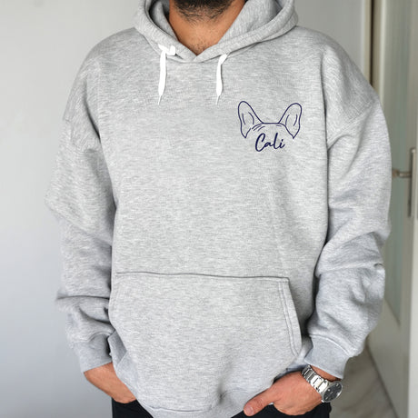 a man wearing a grey sweatshirt with a cat embroidered on it