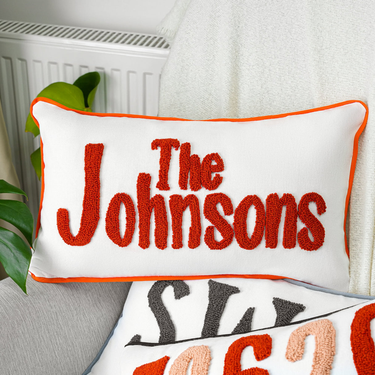 two personalized pillows on a couch with a plant in the background