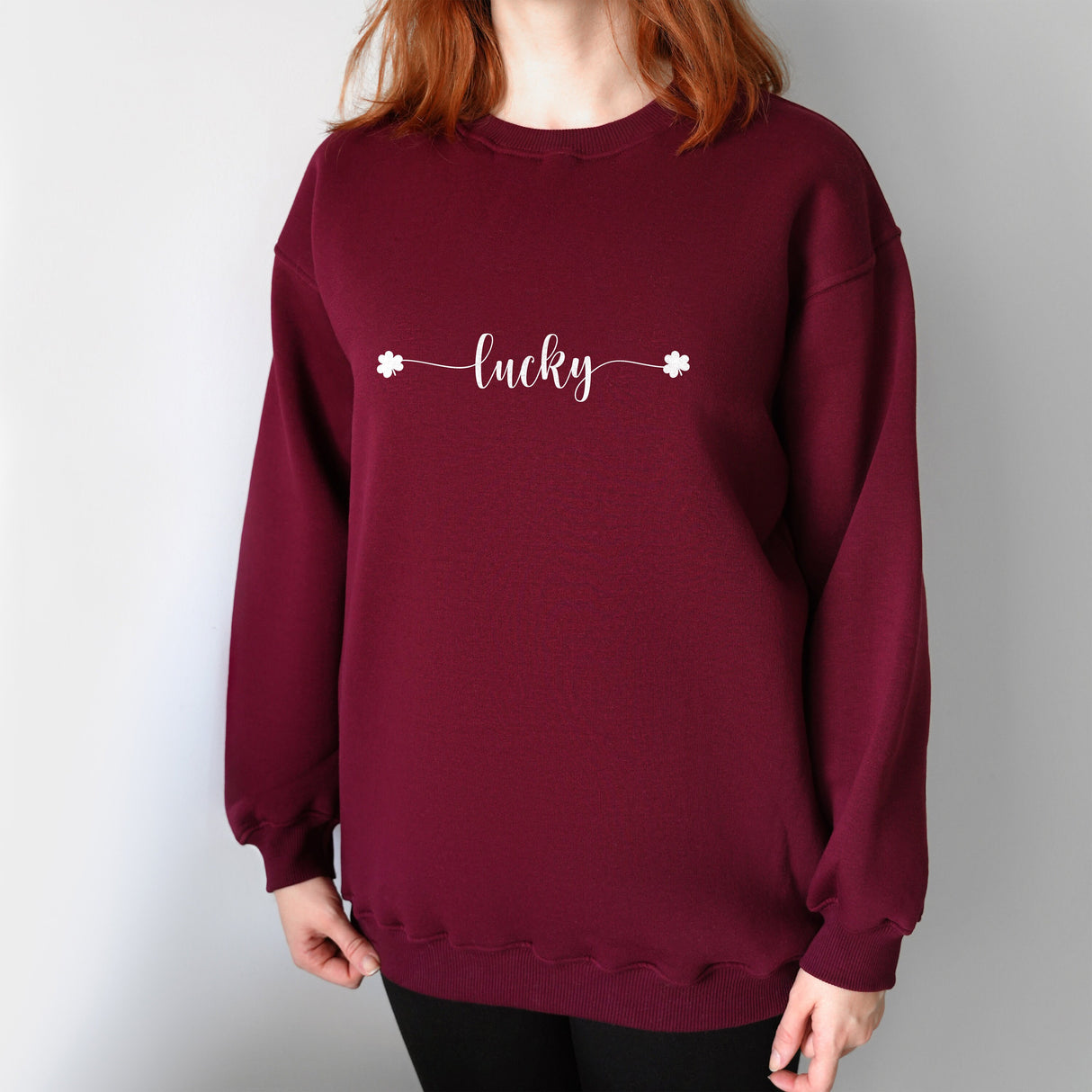 a woman with red hair wearing a burgundy sweatshirt with the word lucky printed on it