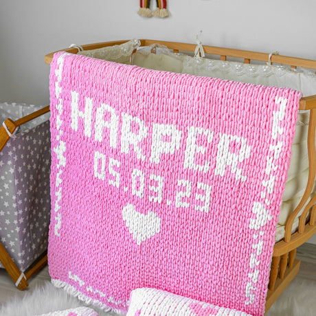 a pink knitted blanket sitting on top of a wooden crib