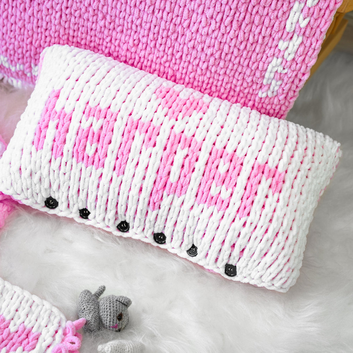 a pink and white knitted pillow next to a stuffed animal