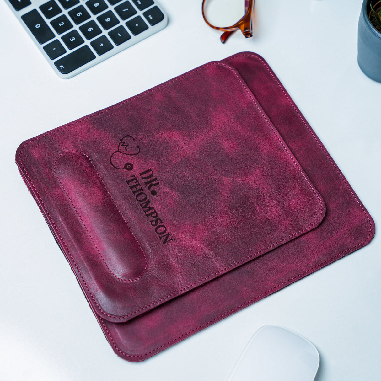 a computer mouse, keyboard, and a leather case on a desk