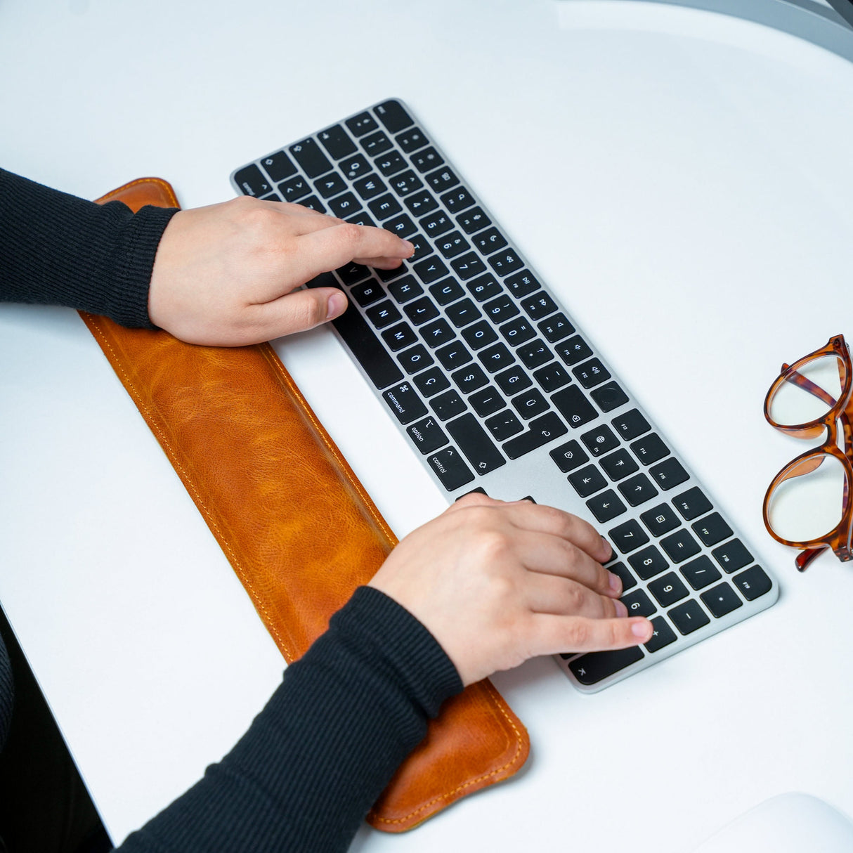 a person typing on a keyboard with a pair of glasses