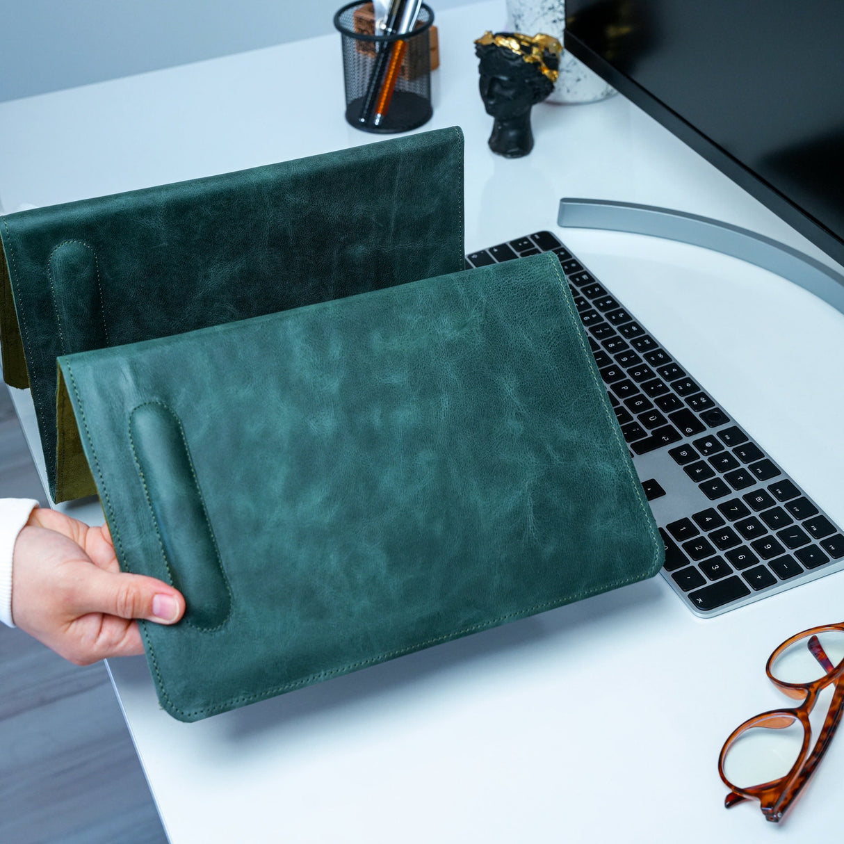 a person holding a green leather case next to a laptop