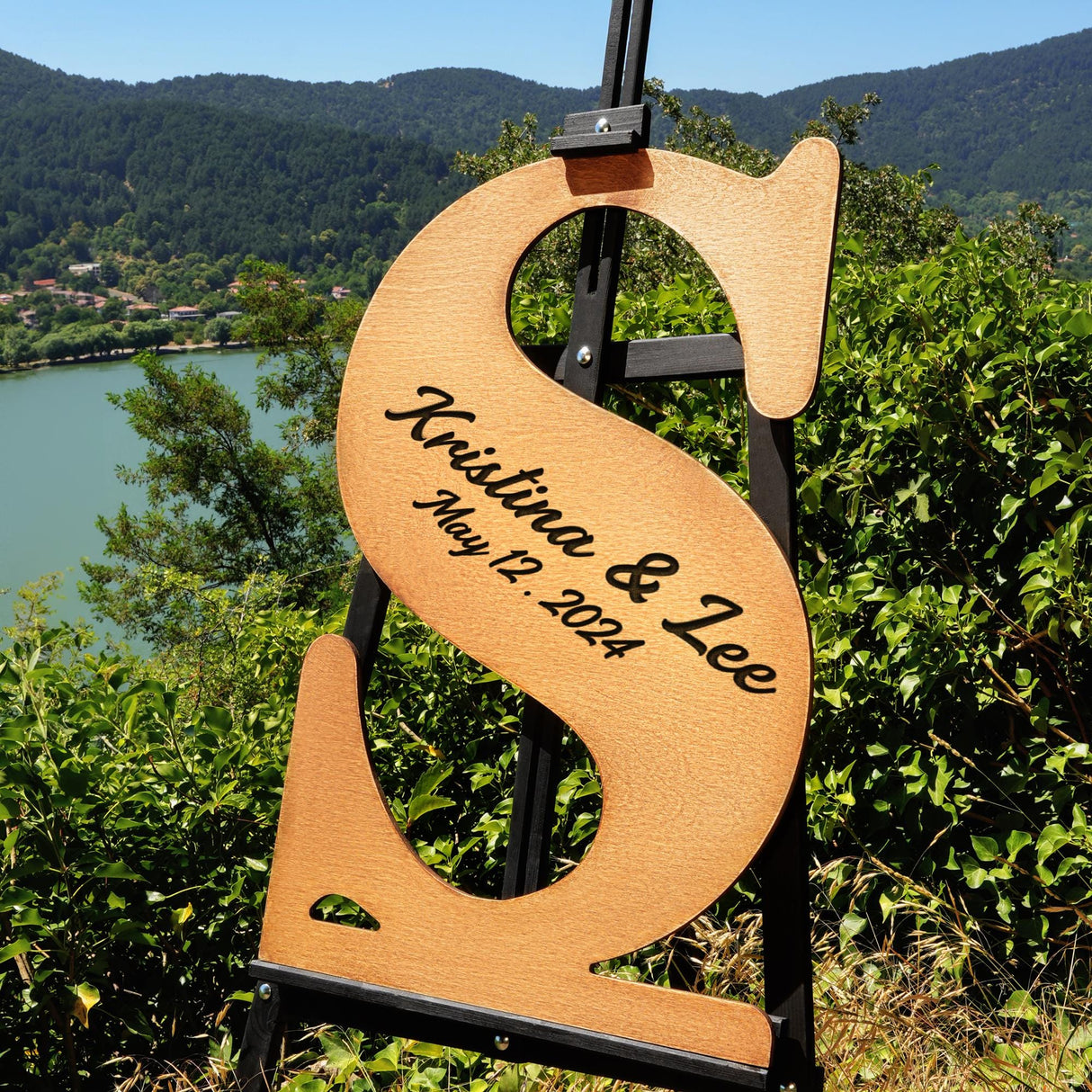 a wooden sign on a metal pole with a lake in the background