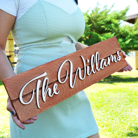 a woman holding a wooden sign that says the williamss