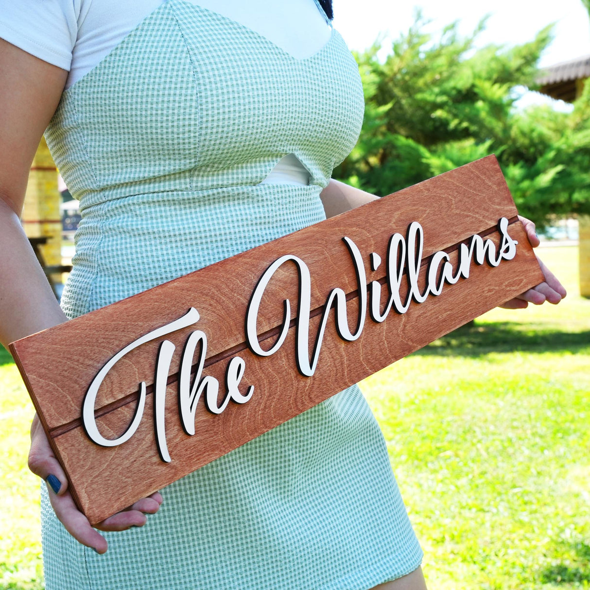 a woman holding a wooden sign that says the williamss