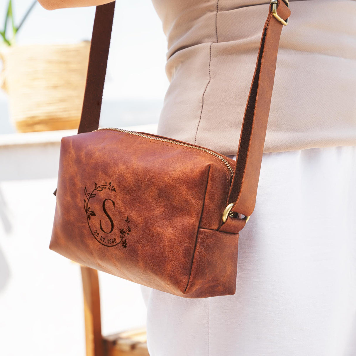 a woman holding a brown purse with a monogrammed letter on it