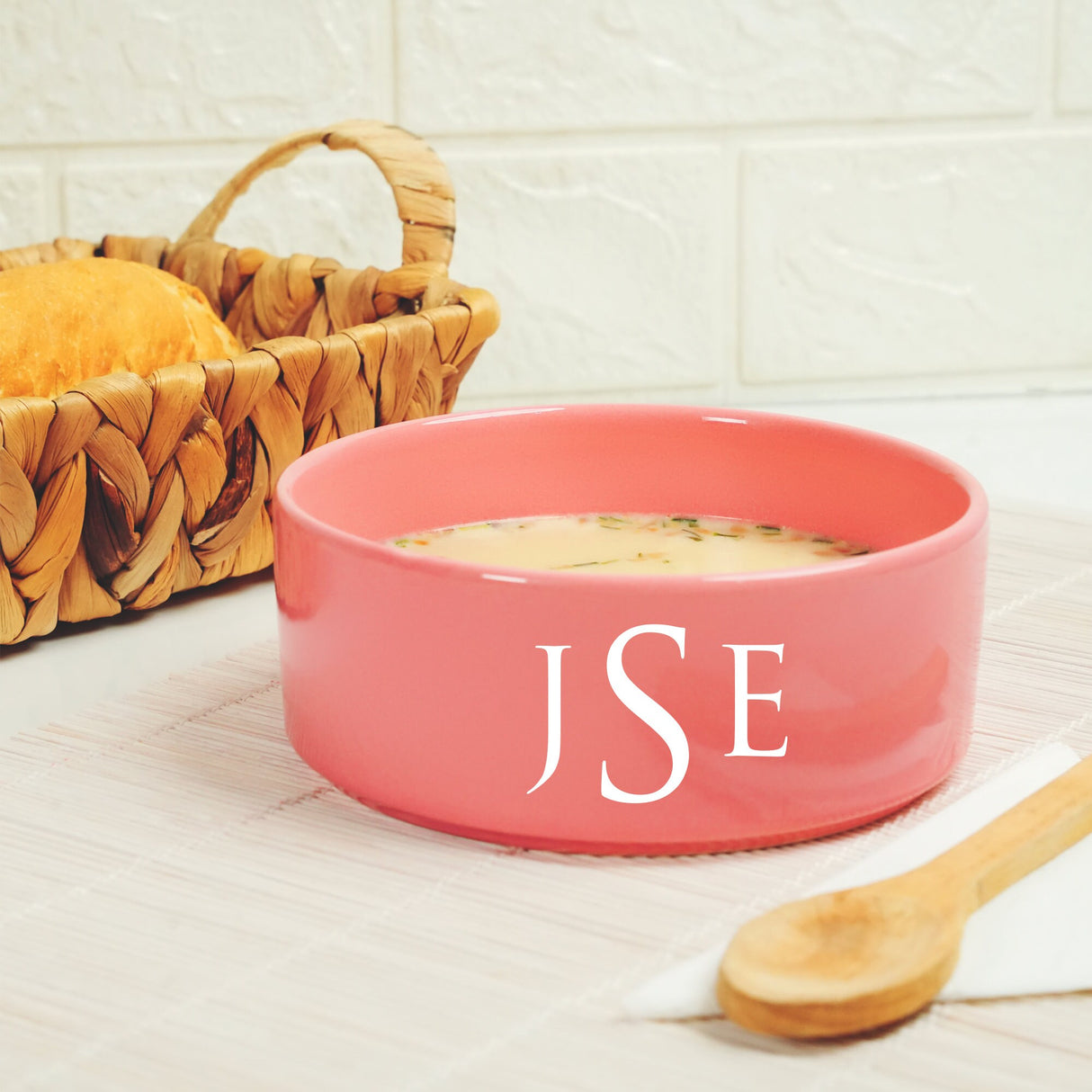 a pink bowl of soup next to a basket of bread