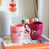 two pink coffee mugs sitting on top of a book