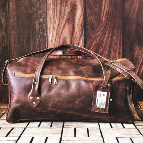 a brown leather duffel bag sitting on top of a tiled floor