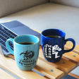 two coffee mugs sitting on a table next to a laptop