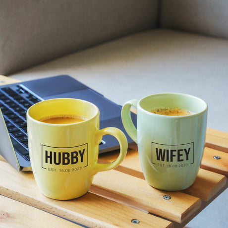 two mugs of coffee sit next to a laptop