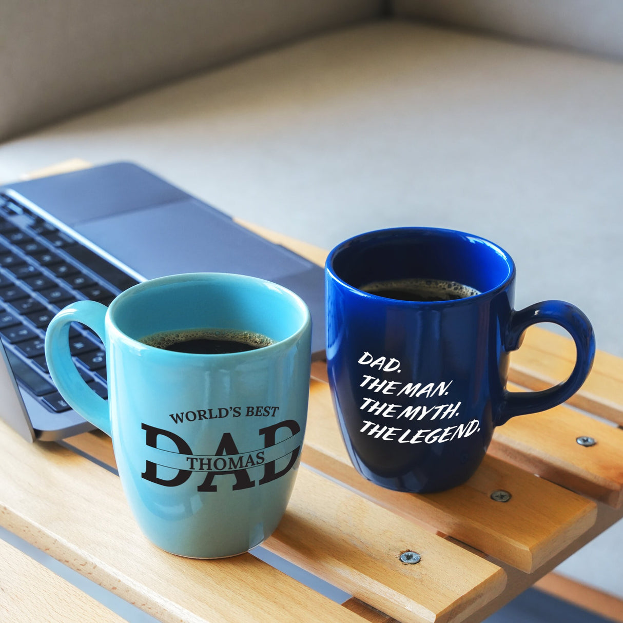 two coffee mugs sitting on a table next to a laptop