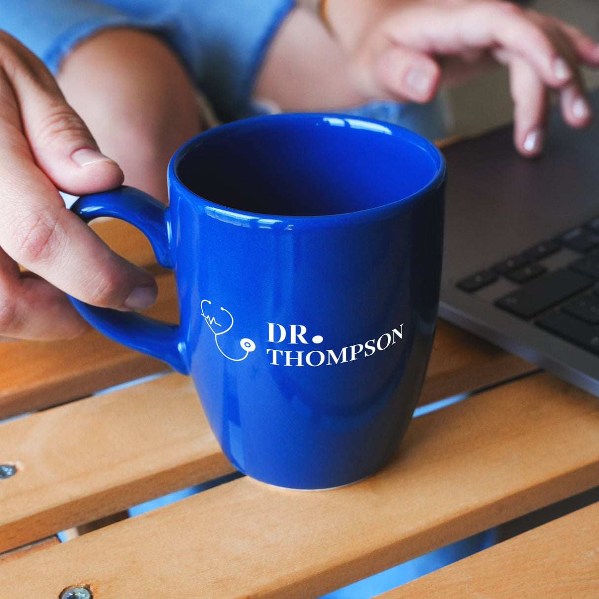 a person holding a blue coffee mug in front of a laptop