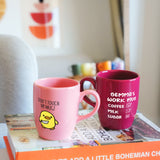 two pink coffee mugs sitting on top of a stack of books